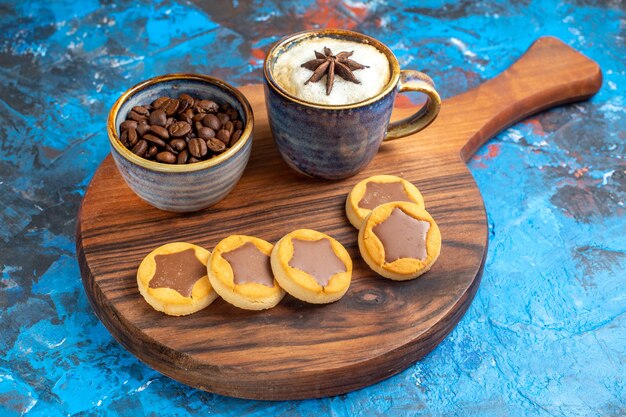 Vista lateral cercana dulces una taza de café, galletas y granos de café en el tablero