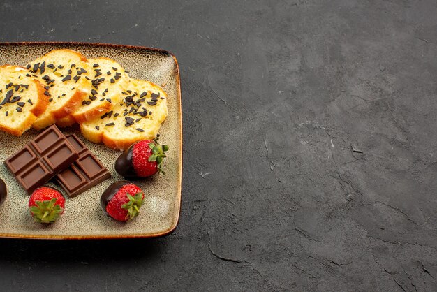 Vista lateral cercana de fresas y tarta de fresas cubiertas de chocolate y tarta con chocolate en el lado izquierdo de la mesa