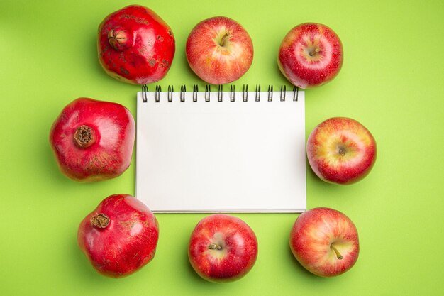 Vista lateral cercana frutas granadas manzanas alrededor de cuaderno blanco sobre fondo verde