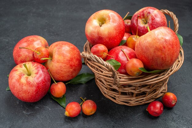 Vista lateral cercana frutas rojo-amarillo manzanas y cerezas en la canasta