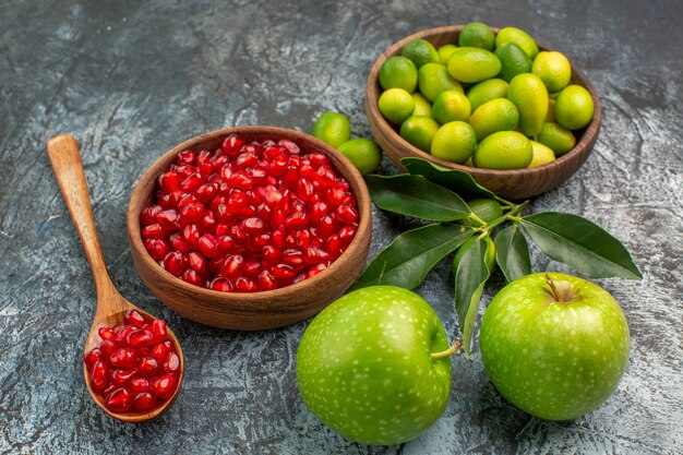 Vista lateral cercana frutas semillas de granada cuchara manzanas cítricos en el tazón de fuente