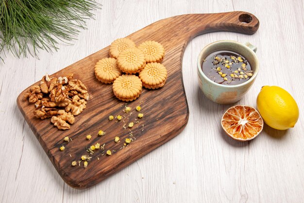 Vista lateral cercana galletas una taza de té y limón junto a la tabla de madera con nueces y apetitosas galletas y ramas de árboles de Navidad