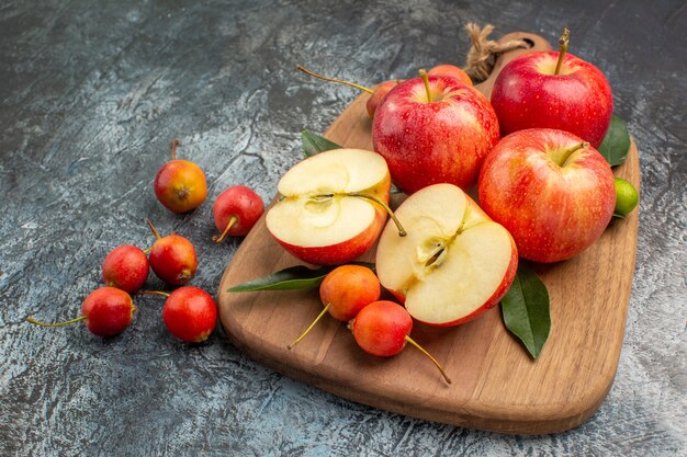 Vista lateral cercana manzanas la tabla de cortar con manzanas cerezas con hojas