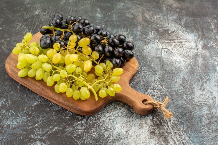 Foto gratuito vista lateral cercana tabla de cortar de madera de uvas y racimos de las apetitosas uvas