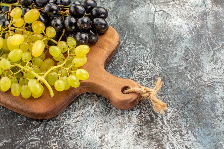 Foto gratuito vista lateral cercana tabla de cortar de madera de uvas y uvas verdes y negras