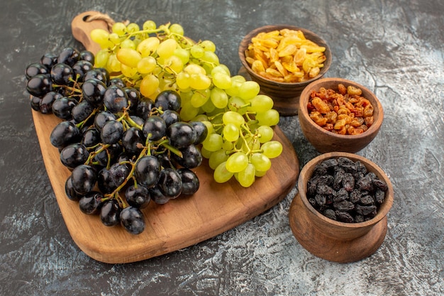 Vista lateral cercana uvas tres tazones de frutos secos uvas sabrosas en la tabla de cortar