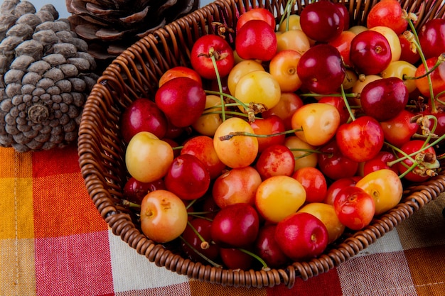 Foto gratuita vista lateral de cerezas maduras más lluviosas en una cesta de mimbre sobre tela escocesa