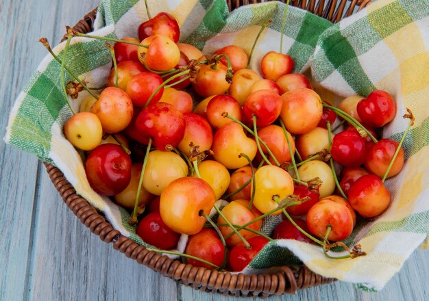 Vista lateral de cerezas maduras más lluviosas en una cesta de mimbre en superficie rústica