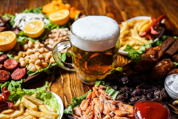 Vista lateral cerveza aperitivos salchichas guisantes semillas y papas fritas con rodajas de limón en un soporte con un vaso de cerveza