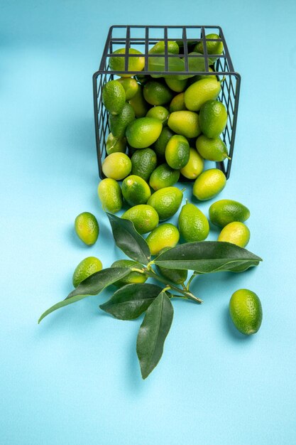 Vista lateral de la cesta de frutas lejanas de frutas cítricas de color amarillo verdoso con hojas sobre la mesa azul