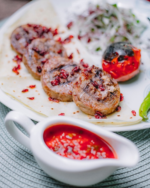 Vista lateral de champiñones rellenos con queso pollo y nueces decoradas con agracejo en lavash servido con tomate a la parrilla y cebolla con hierbas en un plato