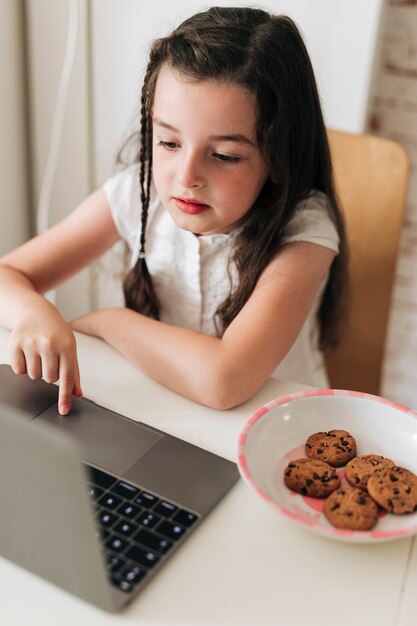 Vista lateral chica con galletas mirando portátil