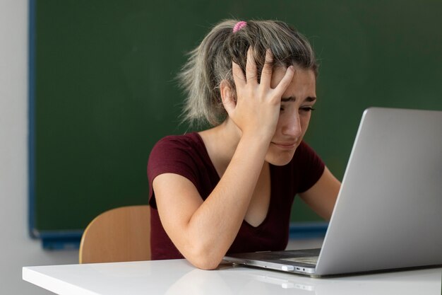 Vista lateral chica triste en la escuela con laptop