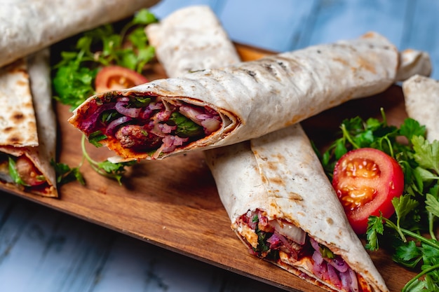 Foto gratuita vista lateral chuleta de carne envuelta en pitta con cebolla roja salsa de tomate verde y tomate fresco en una bandeja