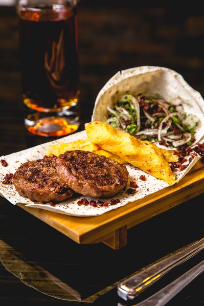 Vista lateral chuletas de carne a la parrilla con cebolla de papa lula y granada en pan de pita con un vaso de cerveza en la mesa