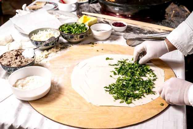 Vista lateral, el cocinero está cocinando cutab con verduras en un tablero con ingredientes