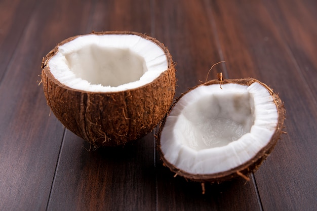 Vista lateral de cocos marrones y mitades frescas sobre una superficie de madera
