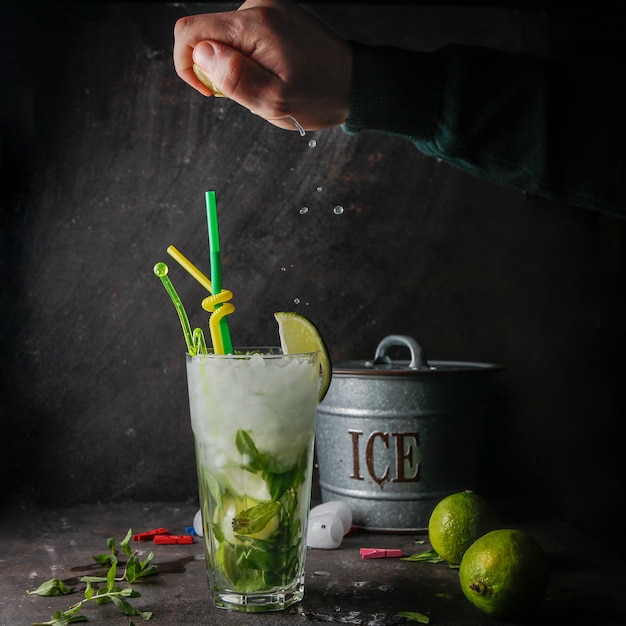 Vista lateral cóctel mojito con menta, limón, hielo, cubo de hielo