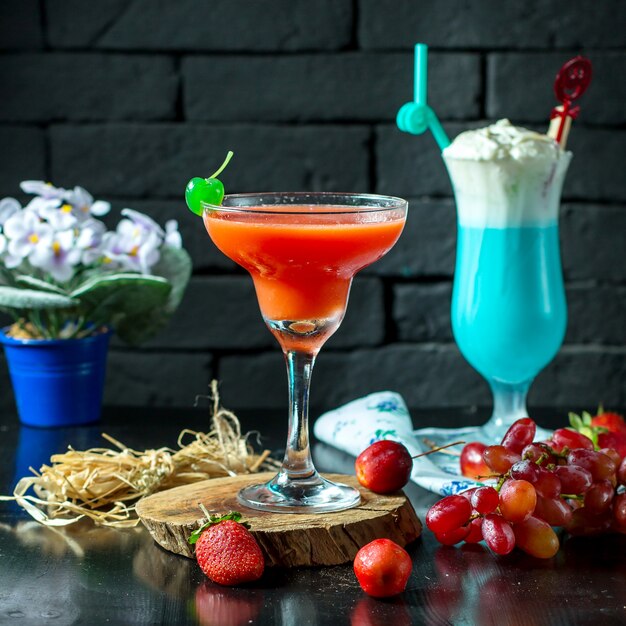 Vista lateral del cóctel rojo en vaso con frutas frescas en la mesa de madera