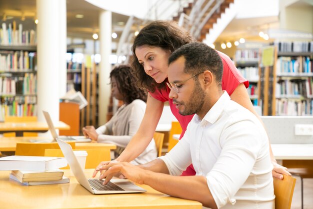 Vista lateral de colegas que trabajan con una computadora portátil en la biblioteca