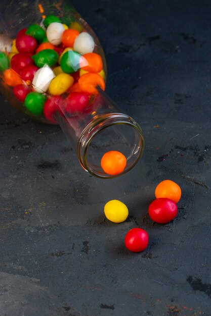 Vista lateral de coloridos dulces en una botella de vidrio sobre negro