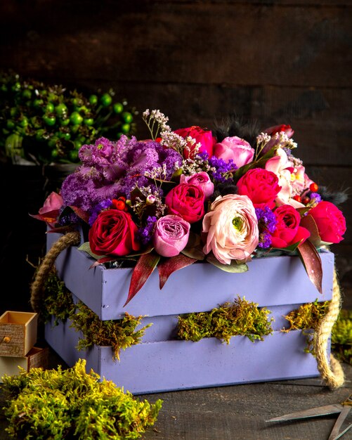 Vista lateral de la composición de flores de rosas de color rosa y lila en caja de madera