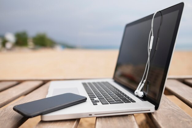 Vista lateral de la computadora portátil en la silla de playa con teléfono inteligente