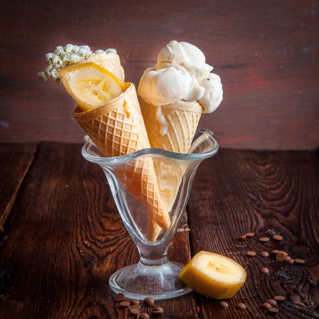 Vista lateral conos de waffle con helado de plátano y rodajas de plátano y gotas de chocolate en una taza de helado