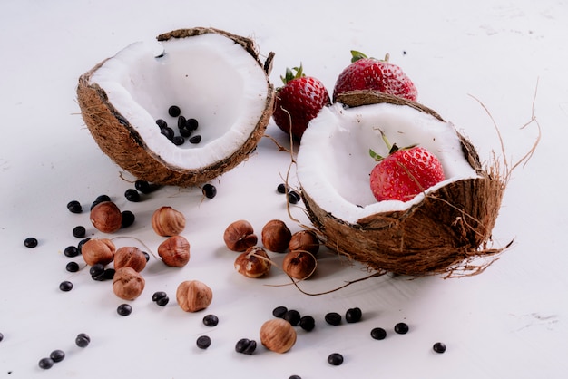 Vista lateral de corte de coco y nueces semillas de pimienta negra con fresas en mesa blanca