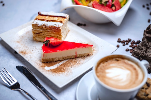 Vista lateral corteza de crujiente de tarta de queso con crema de queso mermelada de fresa y una taza de café sobre la mesa