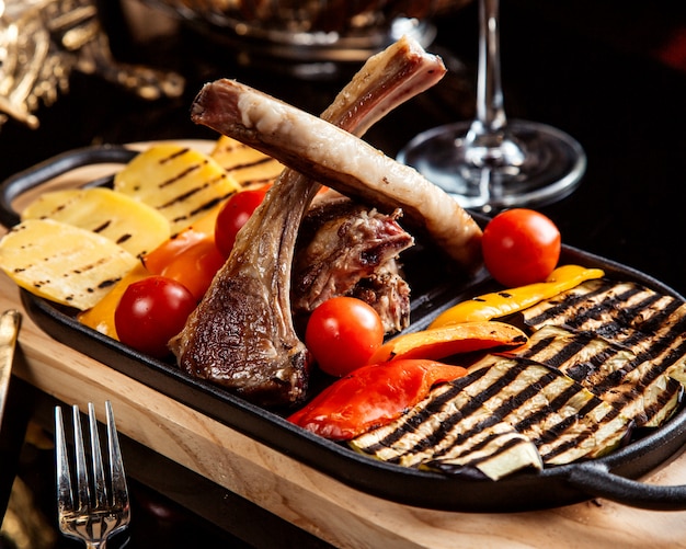 Vista lateral de costillas de cordero fritas adornadas con verduras a la parrilla y tomates frescos sobre la mesa