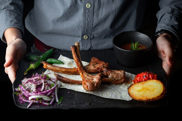 Vista lateral costillas costillas a la parrilla sobre pan de pita con papas al horno, pimientos, tomate y salsa