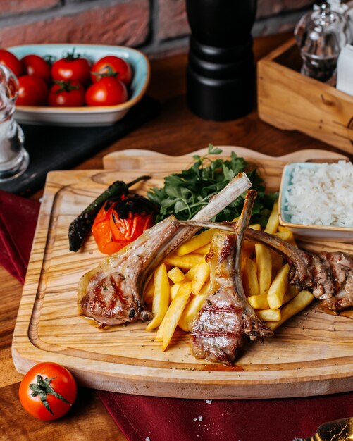 Vista lateral de costillas kebab con papas fritas arroz y verduras sobre una plancha de madera