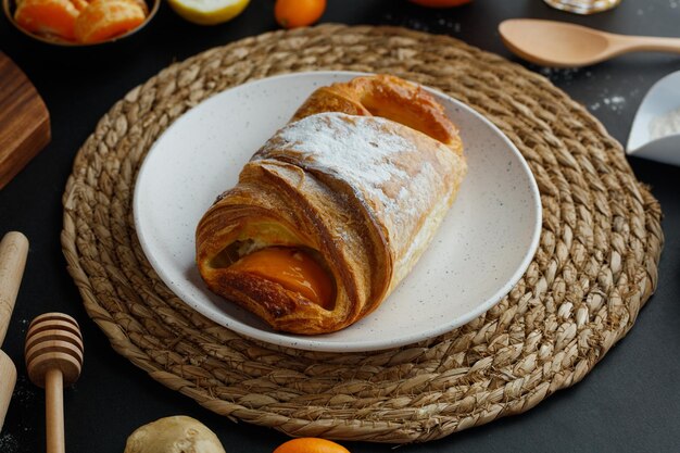 Foto gratuita vista lateral del croissant en plato sobre salvamanteles con limón, mandarina, harina de kumquat, jengibre con cuchara, cucharón de miel y rodillo sobre fondo negro