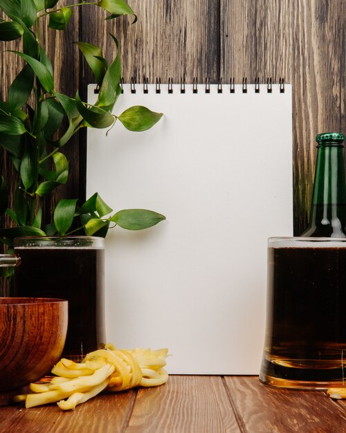 Vista lateral de un cuaderno de dibujo y dos jarras de cerveza con queso en hilo rústico