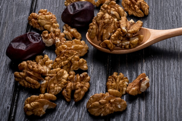 Vista lateral de una cuchara de madera con nueces y frutos de dátiles secos dulces en rústico