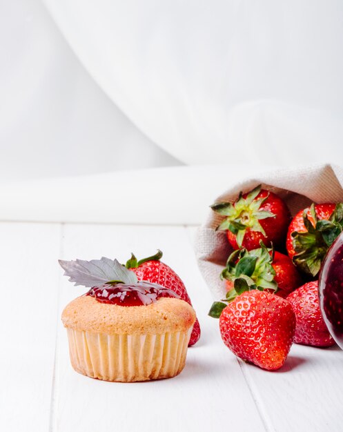 Vista lateral cupcake con mermelada de fresa albahaca y fresa fresca sobre fondo blanco.