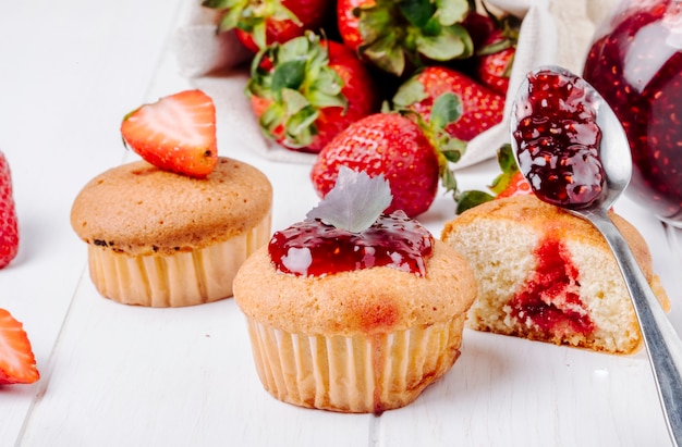 Vista lateral cupcakes con mermelada de fresa albahaca y fresa fresca sobre fondo blanco.