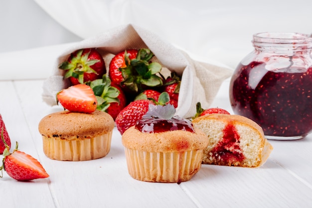 Vista lateral cupcakes con mermelada de fresa albahaca y fresa fresca sobre fondo blanco.