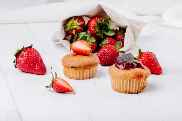 Vista lateral cupcakes con mermelada de fresa albahaca y fresa fresca sobre fondo blanco.