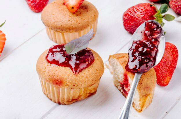 Vista lateral cupcakes con mermelada de fresa y albahaca sobre fondo blanco.