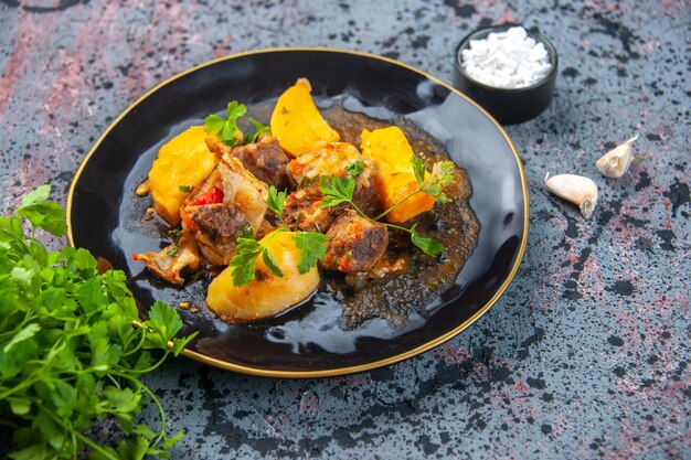 Vista lateral de la deliciosa cena con patatas de carne servidas con verde en un plato negro y sal de ajo sobre fondo de colores mezcla