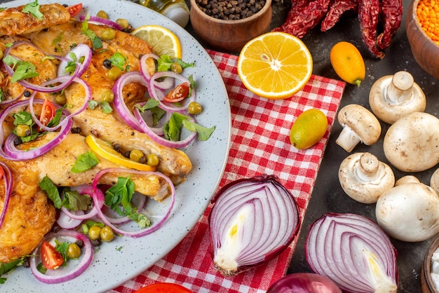 Vista lateral de una deliciosa cena plato de pollo frito con varias especias y alimentos ajos botella de aceite caído limón pimientos secos champiñones kumquats