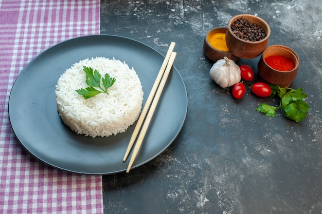 Foto gratuita vista lateral de la deliciosa comida de arroz servida con palillos de madera verde sobre un plato negro sobre una toalla de color púrpura y tomates de ajo de diferentes especias sobre fondo oscuro