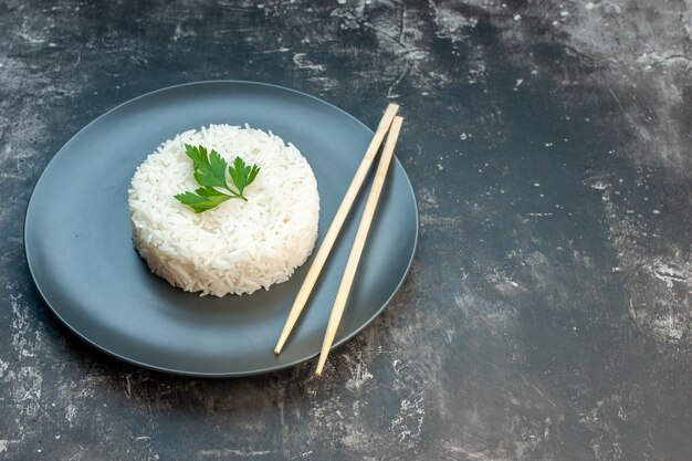 Foto gratuita vista lateral de la deliciosa comida de arroz servida con palillos verdes y en una placa negra en el lado derecho sobre fondo oscuro