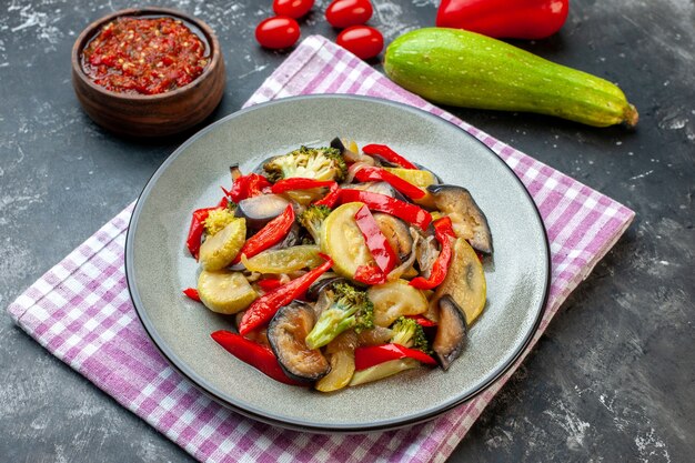 Vista lateral de una deliciosa comida sin carne en un plato sobre una toalla de color púrpura y salsa de verduras sobre fondo oscuro