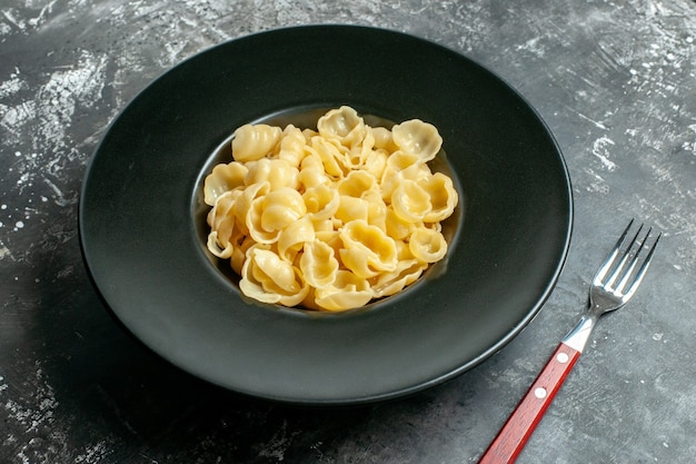 Vista lateral de la deliciosa conchiglie en un plato negro y un cuchillo sobre fondo gris