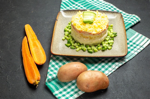 Foto gratuita vista lateral de una deliciosa ensalada servida con pepino picado en zanahorias y papas de toalla verde doblado por la mitad sobre fondo oscuro