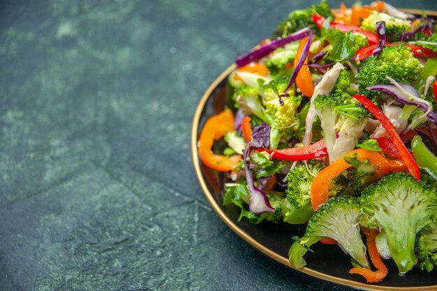 Vista lateral de la deliciosa ensalada vegana en un plato con varias verduras frescas sobre fondo oscuro