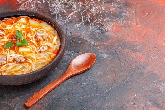 Vista lateral de la deliciosa sopa de fideos con pollo en un recipiente marrón y una cuchara sobre el fondo oscuro